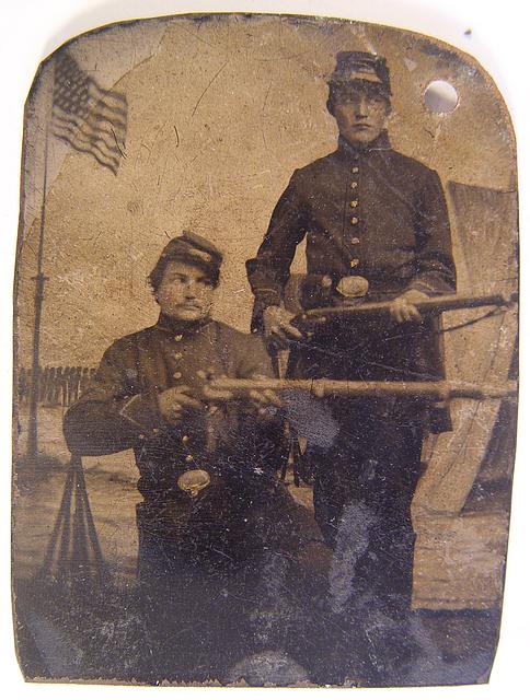 Brothers William and Philip J. Letsinger of Company D, 14th Indiana Regiment posing with rifles in front of Camp Michigan painted backdrop