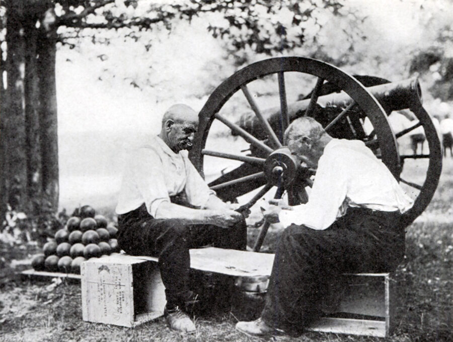 Gettysburg veterans sit next to a cannon and play cards.