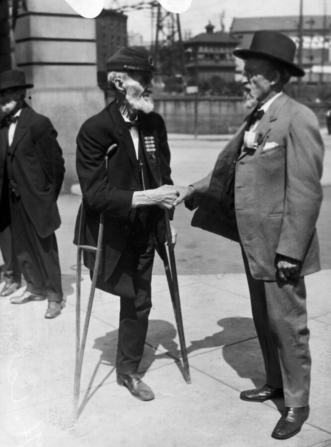 A Union and Confederate veteran shake hands after the reunion at Gettysburg.