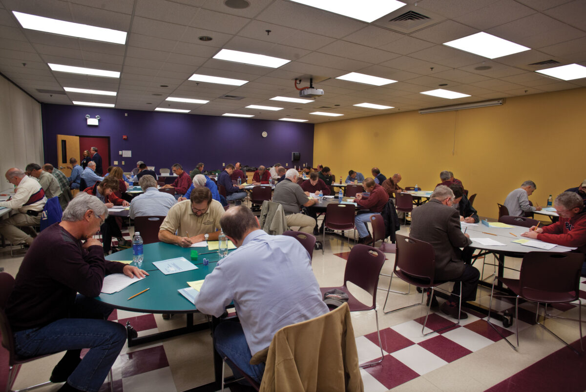Room full of people sitting at circular desks taking an exam.