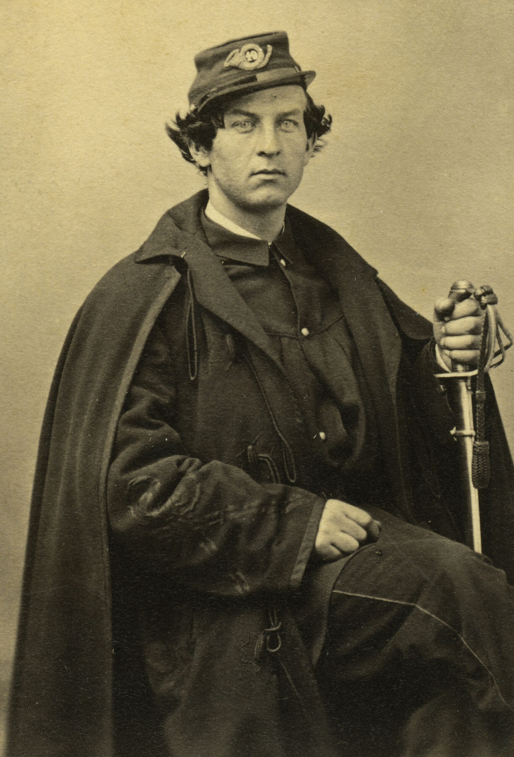 Portrait of John C. White, 2nd Lieutenant, 49th New York Infantry, seated in uniform with cape and sword.